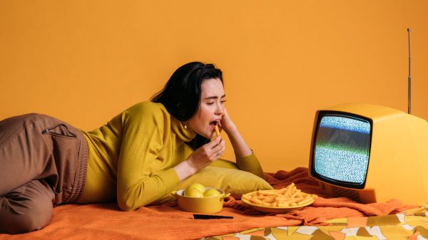 woman in yellow long sleeve shirt watching tv and eatinghi