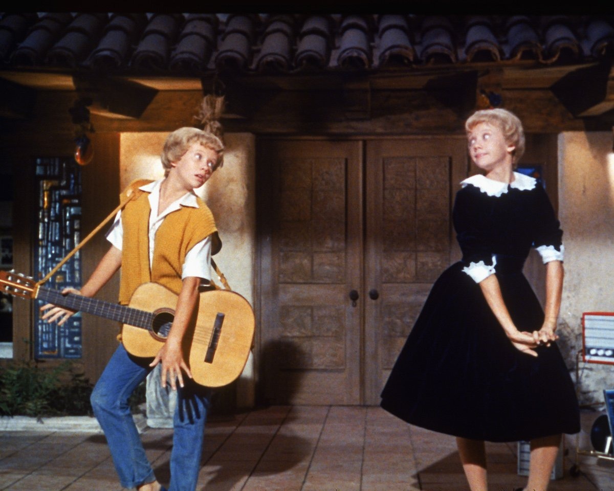 Hayley Mills portraying both twins, Susan and Sharon, in a lively scene from Disney’s 1961 film The Parent Trap. She plays guitar opposite her other character in a playful moment showcasing the film’s innovative split-screen effects.