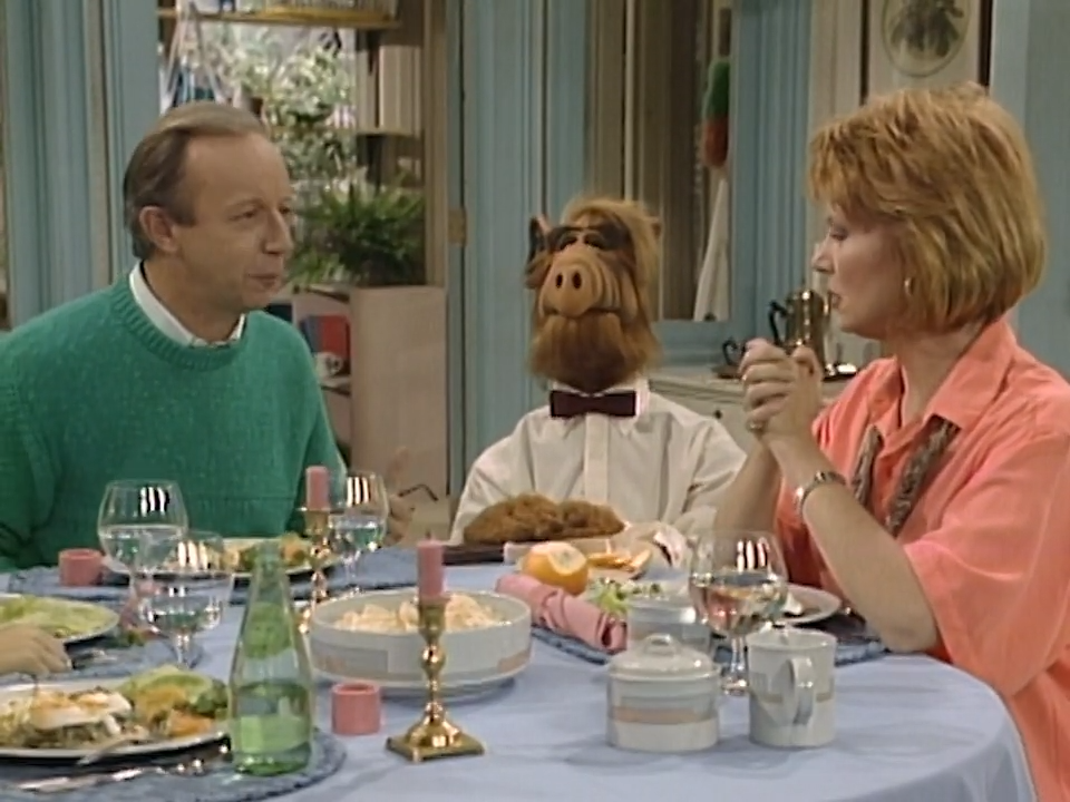 Anne Schedeen as Kate Tanner sits at a dinner table with Max Wright as Willie Tanner and the ALF puppet in a scene from the NBC sitcom "ALF."