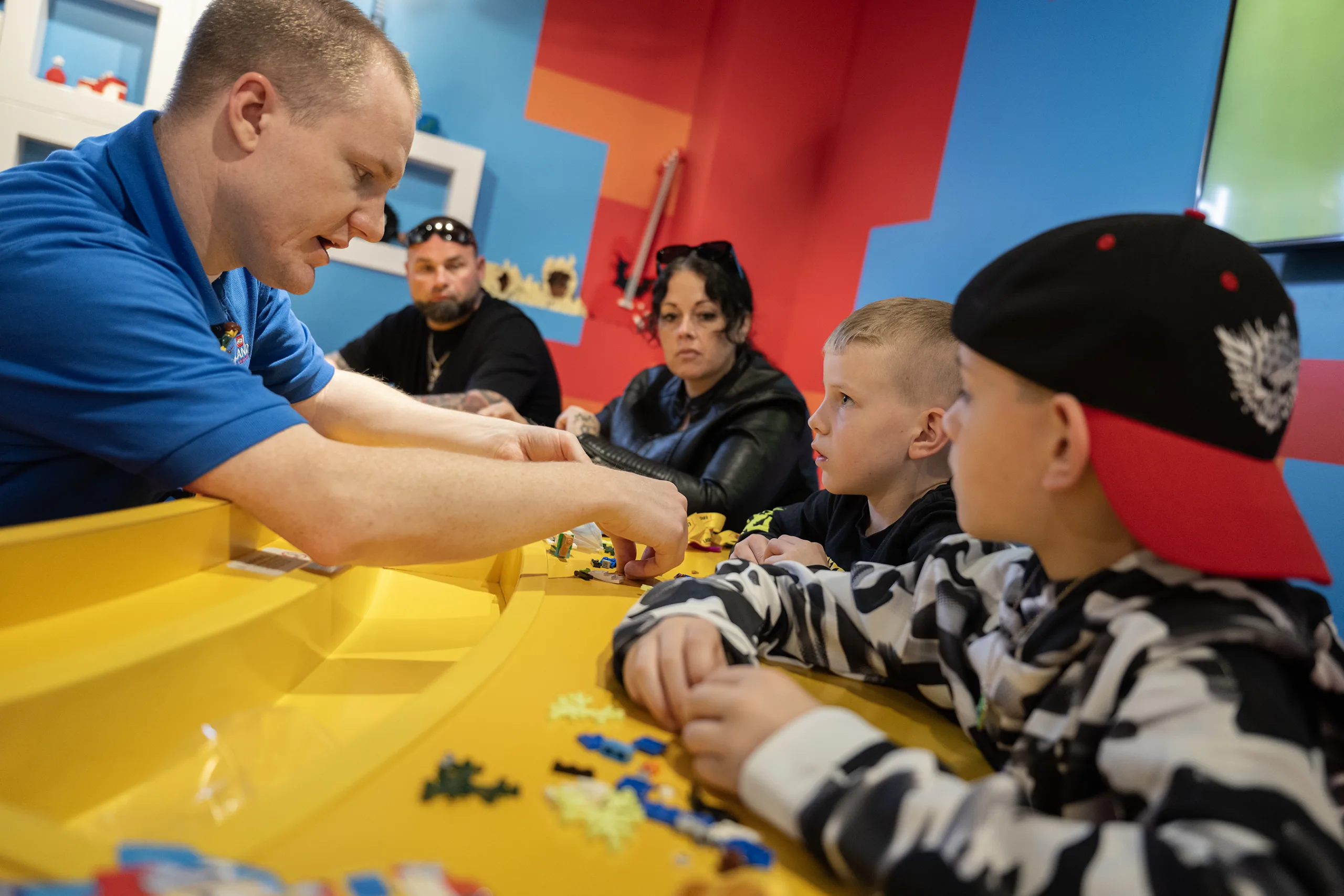 LEGOLAND Discovery Center Master Model Builder assists two children with LEGO pieces at the Creative Workshop table.