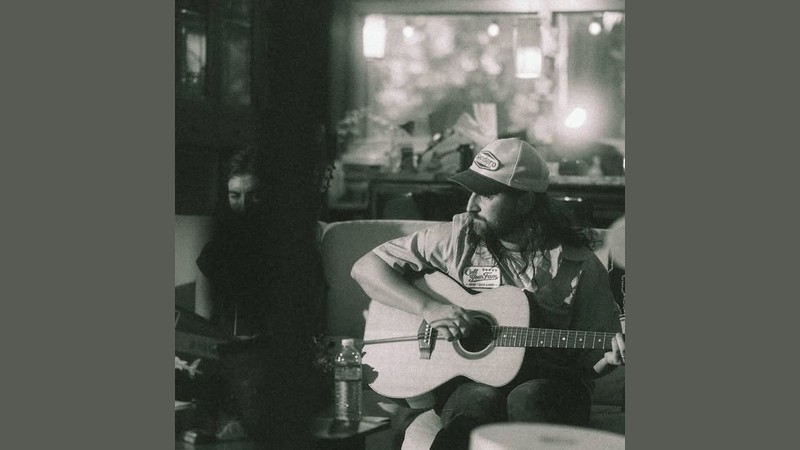 Noah Kahan playing an acoustic guitar in a black-and-white session photo