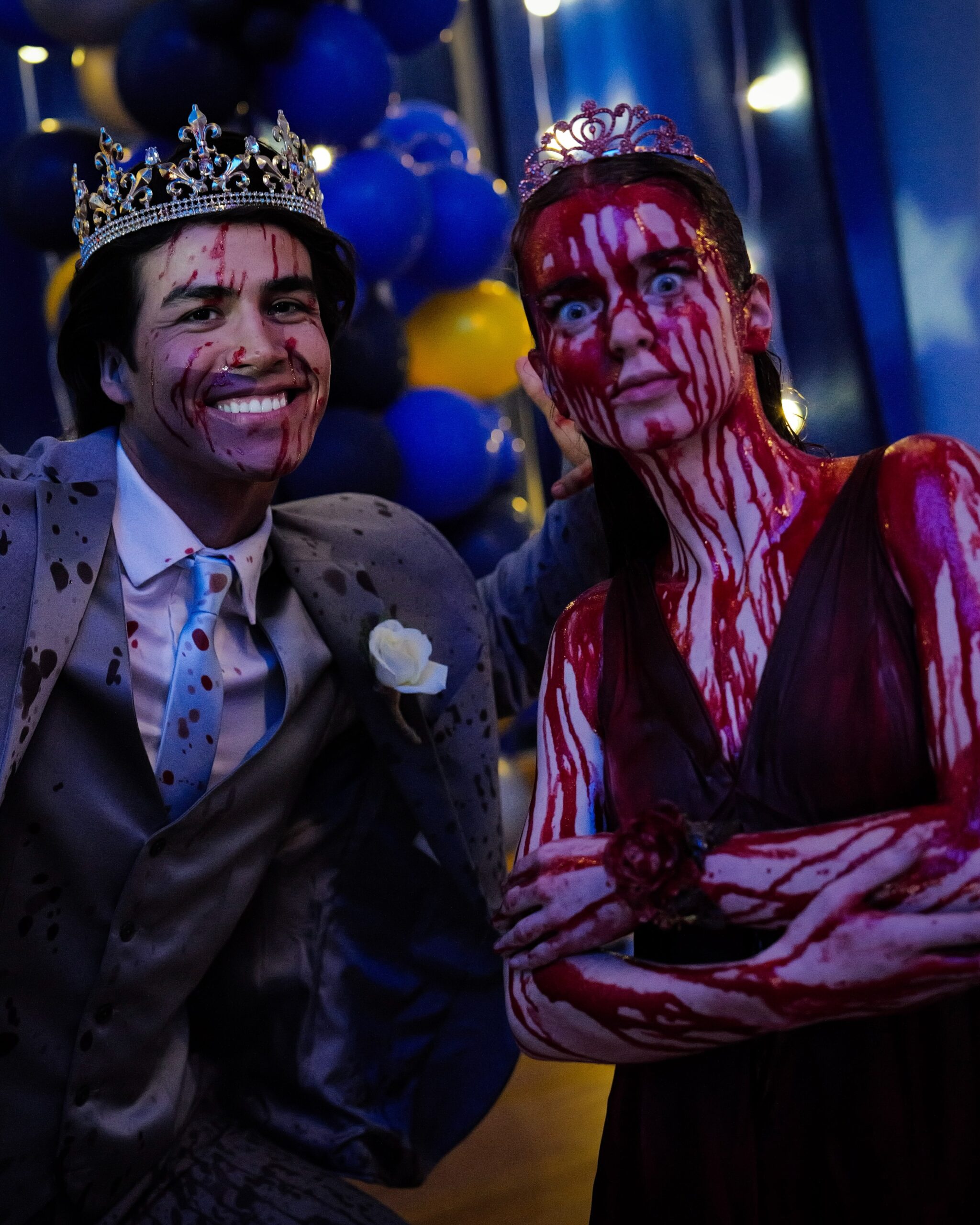 Summer H. Howell as Carrie, covered in stage blood and wearing a tiara, poses beside the prom king at the Carrie prom