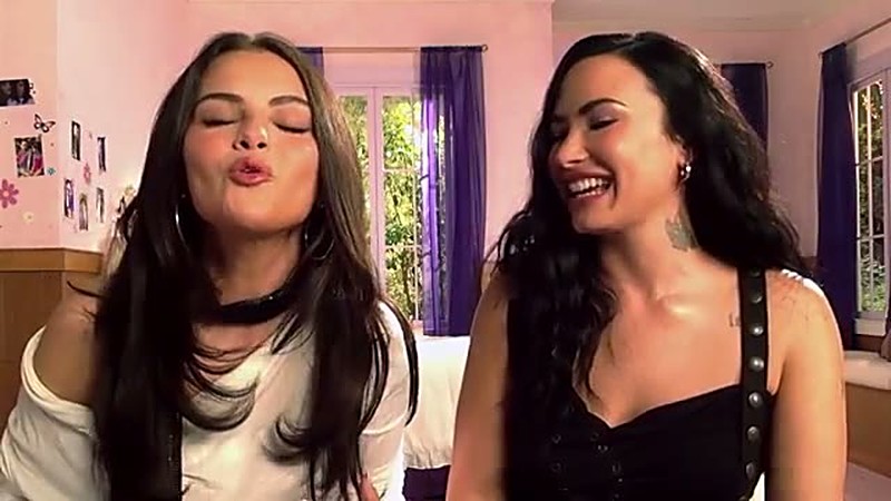Selena Gomez blows a kiss to the camera while Demi Lovato laughs beside her in their Checking In reunion vlog