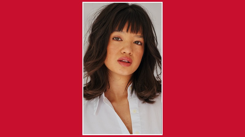 Peyton Elizabeth Lee in a portrait with dark wavy hair and bangs, wearing a white shirt.