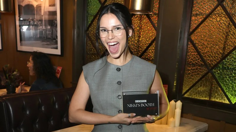 Inde Navarrette smiling and holding the Nikki's Booth plaque at Little Toni's Restaurant