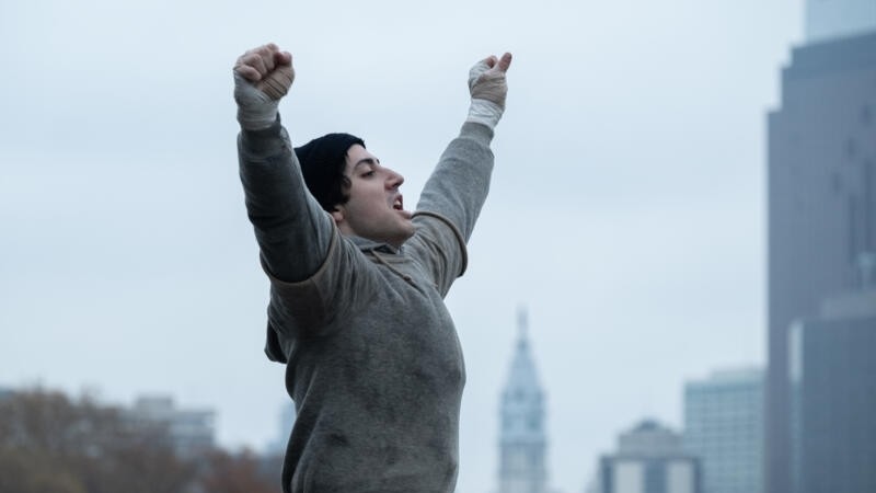 Anthony Ippolito as Rocky Balboa with his arms raised in victory in I Play Rocky