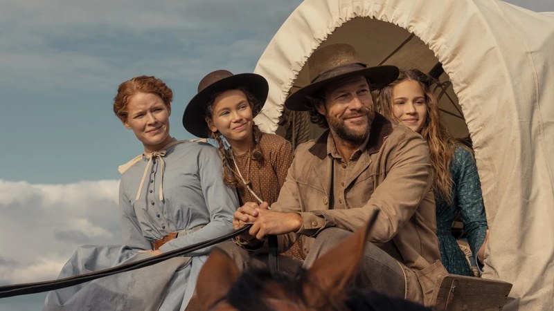 Crosby Fitzgerald, Alice Halsey, Luke Bracey, and Skywalker Hughes as the Ingalls family riding in a covered wagon in Netflix's Little House on the Prairie
