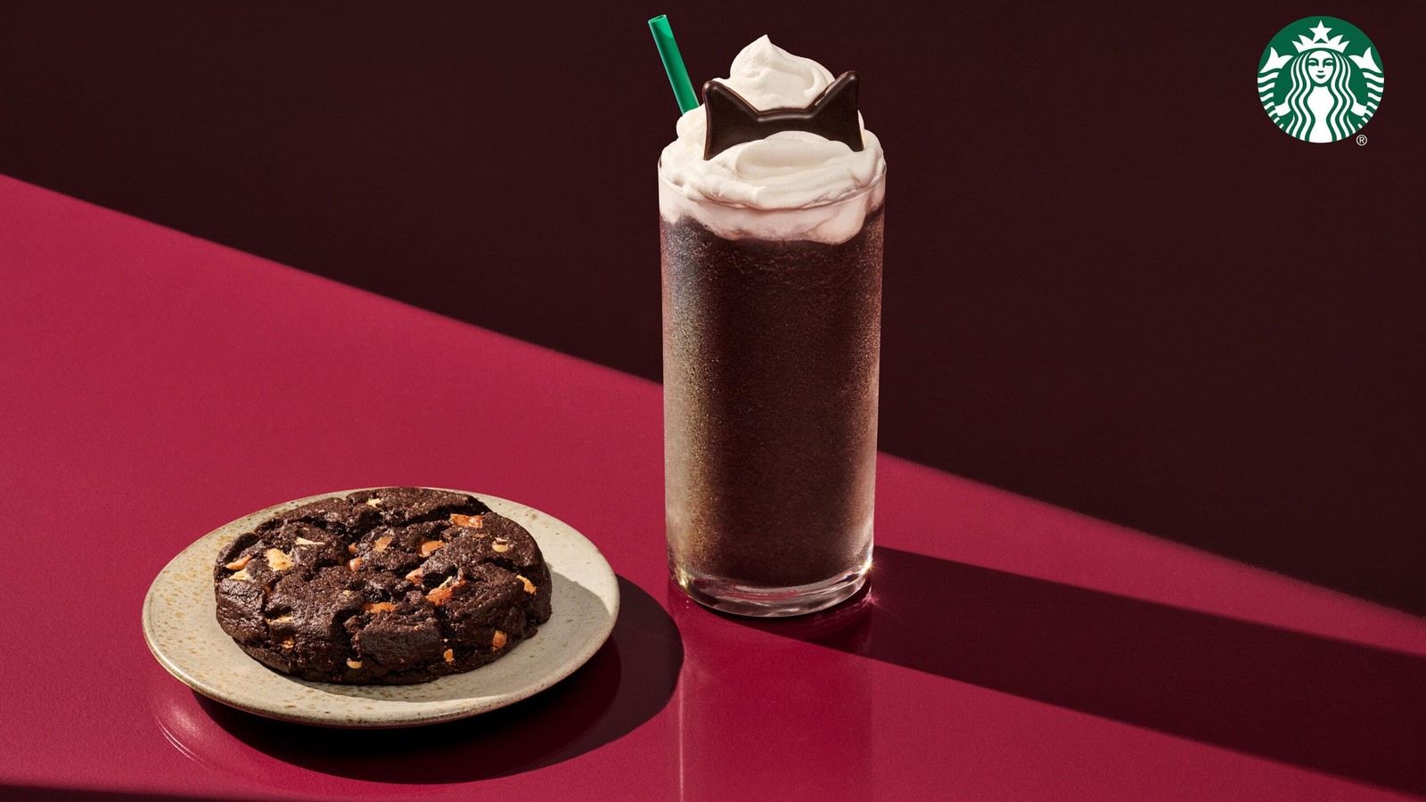 The Starbucks Black Cat Frappuccino topped with whipped cream and chocolatey cat ears, next to the Venti Black Night Cookie